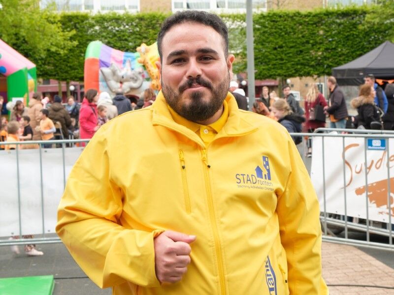 man in een oranje jas staat voor het hek